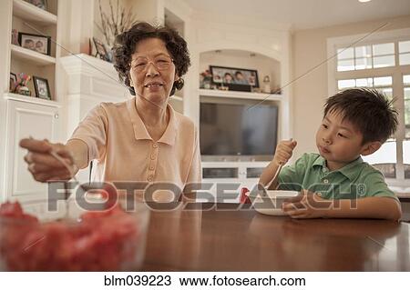 Stock Image - Asian grandmother feeding grandson at table. Fotosearch