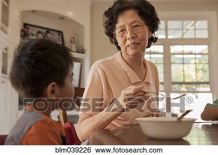 Asian grandmother feeding grandson at table View Large Photo Image Stock Photograph - Asian grandmother feeding grandson at table. Fotosearch