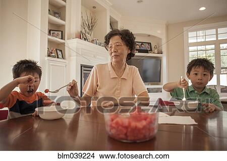 Picture - Asian grandmother feeding grandsons at table. Fotosearch