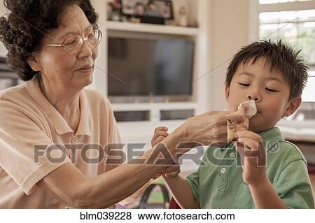 Stock Photo - Asian grandmother wiping face of grandson at table. Fotosearch