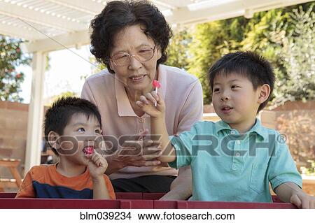 Picture - Asian woman and grandsons relaxing in backyard. Fotosearch