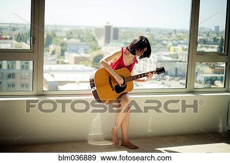 Stock Photo - Asian woman playing guitar in window. Fotosearch