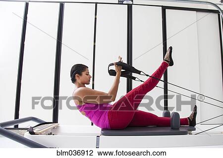 Stock Image - Asian woman using exercise machine in gymnasium. Fotosearch