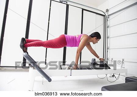 Stock Image - Asian woman using exercise machine in gymnasium. Fotosearch