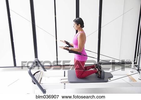 Stock Photo - Asian woman using exercise machine in gymnasium. Fotosearch