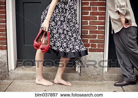 Stock Photo - Barefoot girl holding shoes near boyfriend in doorway. Fotosearch