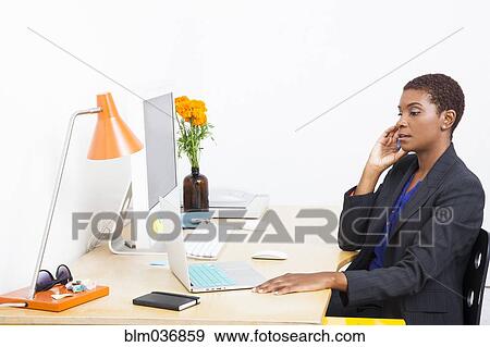 Stock Photo - Black businesswoman talking on cell phone at office desk. Fotosearch