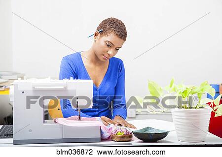 Stock Image - Black dressmaker using sewing machine. Fotosearch