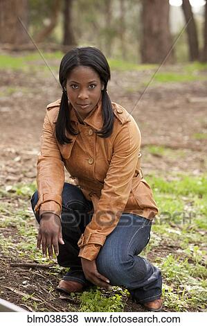 Stock Photo - Black woman crouching in forest. Fotosearch