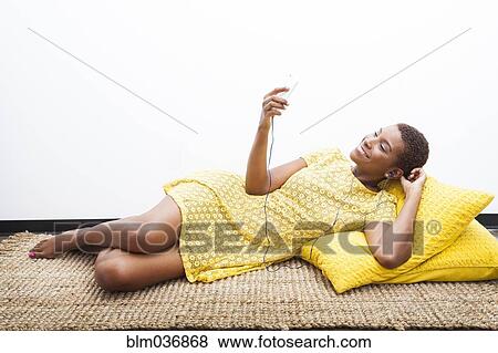 Stock Photo - Black woman listening to mp3 player on carpet. Fotosearch