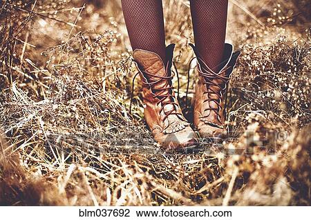 Stock Image - Boots of Caucasian teenage girl standing in tall grass. Fotosearch