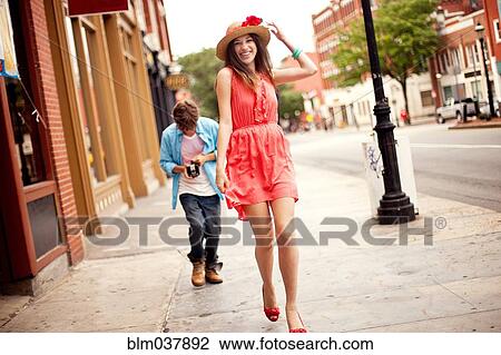 Stock Image - Boy photographing girlfriend on city sidewalk. Fotosearch
