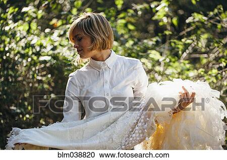 Bride holding wedding gown in garden View Large Photo Image Stock Image - Bride holding wedding gown in garden. Fotosearch