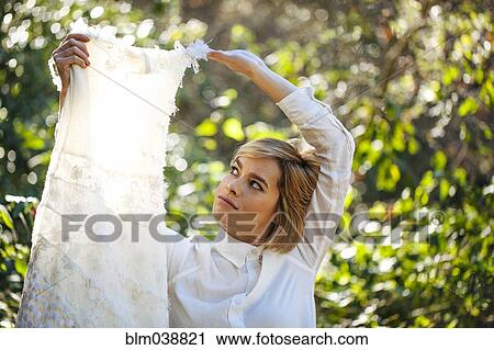 Stock Image - Bride holding wedding gown in garden. Fotosearch