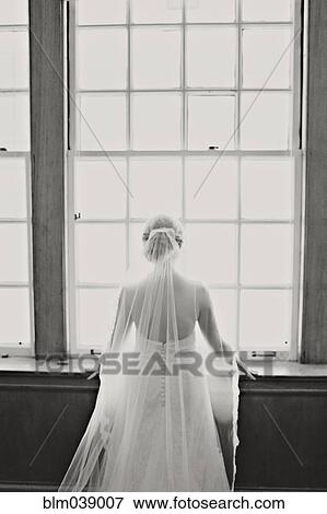 Stock Photo - Bride in veil and wedding gown standing at window. Fotosearch