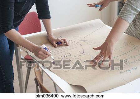 Stock Image - Businesswomen sketching diagram in office. Fotosearch