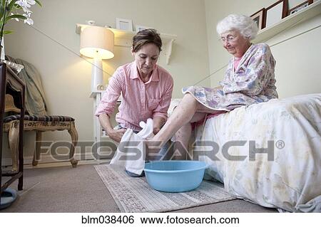 Stock Photograph - Caregiver washing foot of older woman in bedroom. Fotosearch