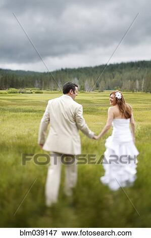 Stock Photo - Caucasian bride and groom walking in rural field. Fotosearch