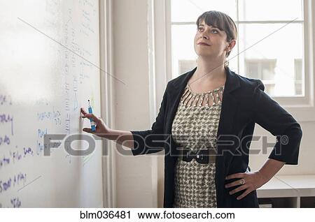 Stock Image - Caucasian businesswoman reading whiteboard in office. Fotosearch