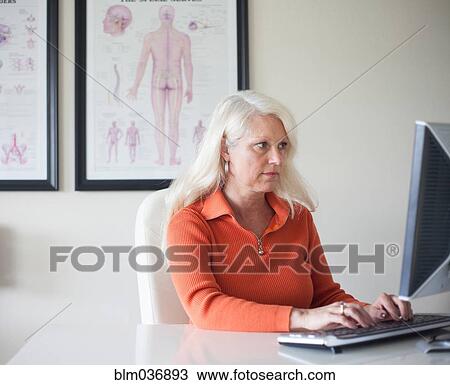 Stock Image - Caucasian chiropractor working at computer. Fotosearch