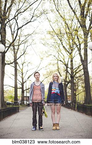 Stock Image - Caucasian couple standing in park with skateboard. Fotosearch