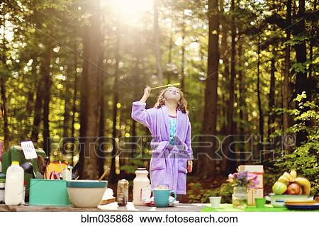 Stock Photo - Caucasian girl blowing bubbles in forest. Fotosearch