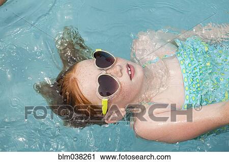 Stock Image - Caucasian girl floating in swimming pool. Fotosearch