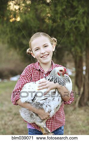 Stock Image - Caucasian girl holding chicken on farm. Fotosearch
