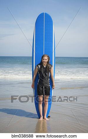 Stock Photo - Caucasian girl holding paddleboard on beach. Fotosearch