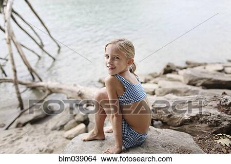 Picture - Caucasian girl in bikini sitting by remote lake. Fotosearch