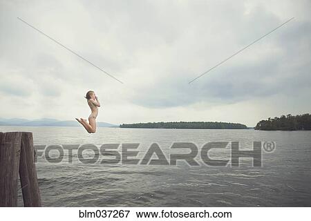 Stock Photo - Caucasian girl jumping in remote lake. Fotosearch