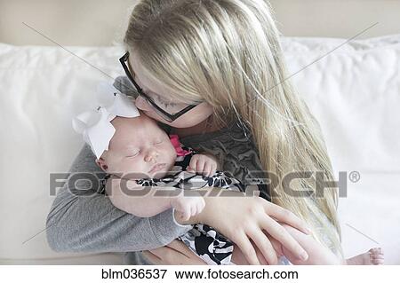 Stock Photo - Caucasian girl kissing newborn sister on sofa. Fotosearch