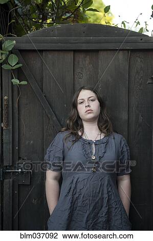 Stock Image - Caucasian girl leaning on wooden gate. Fotosearch