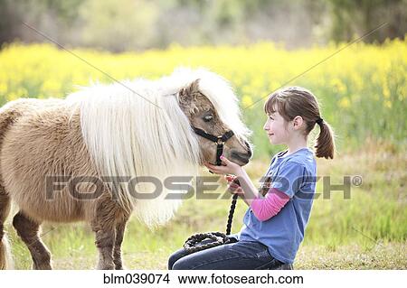 Picture - Caucasian girl petting pony in rural field. Fotosearch