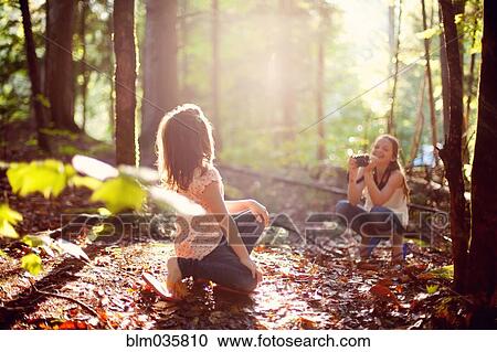 Stock Image - Caucasian girl photographing sister in forest. Fotosearch