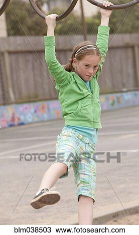 Stock Image - Caucasian girl playing on monkey bars at playground. Fotosearch
