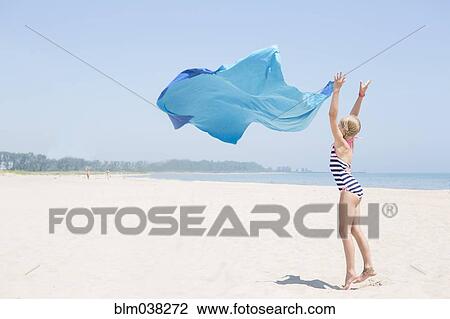 Stock Image - Caucasian girl playing with fabric on beach. Fotosearch