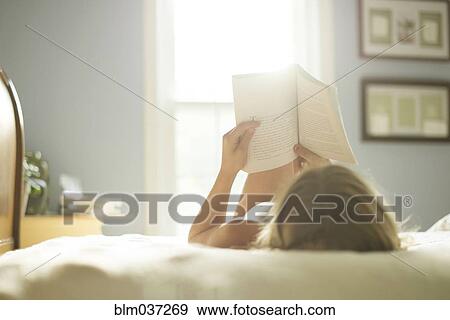 Stock Photo - Caucasian girl reading book on bed. Fotosearch