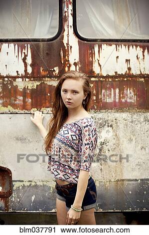 Stock Image - Caucasian girl standing near dilapidated bus. Fotosearch