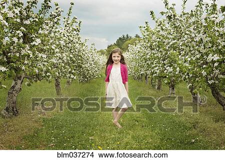 Picture - Caucasian girl walking in blooming orchard. Fotosearch