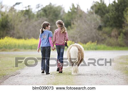 Caucasian girls walking pony on dirt path View Large Photo Image Stock Image - Caucasian girls walking pony on dirt path. Fotosearch