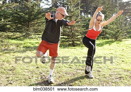 Stock Image - Caucasian man exercising with trainer in field. Fotosearch