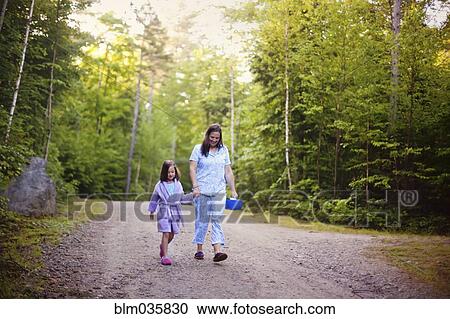 Stock Image - Caucasian mother and daughter walking on dirt road. Fotosearch