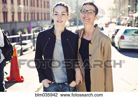 Stock Image - Caucasian mother and daughter walking on city sidewalk. Fotosearch