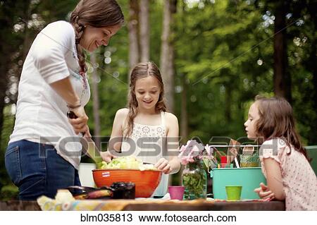 Stock Image - Caucasian mother and daughters cooking outdoors. Fotosearch