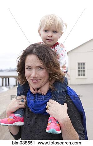 Stock Image - Caucasian mother carrying daughter on shoulders. Fotosearch