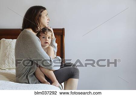Stock Image - Caucasian mother hugging son on bed. Fotosearch