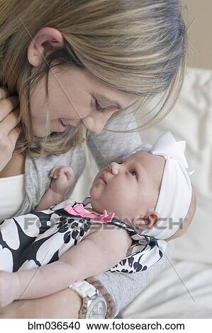 Stock Image - Caucasian mother kissing newborn daughter on sofa. Fotosearch