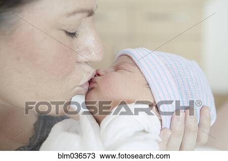 Stock Image - Caucasian mother kissing newborn daughter. Fotosearch