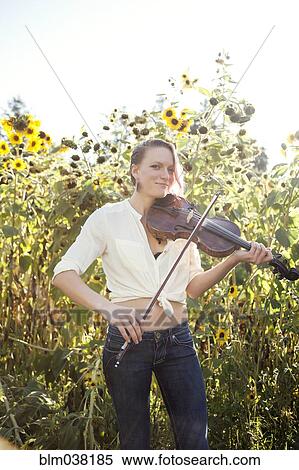 Stock Photography - Caucasian musician playing violin in sunflower garden. Fotosearch